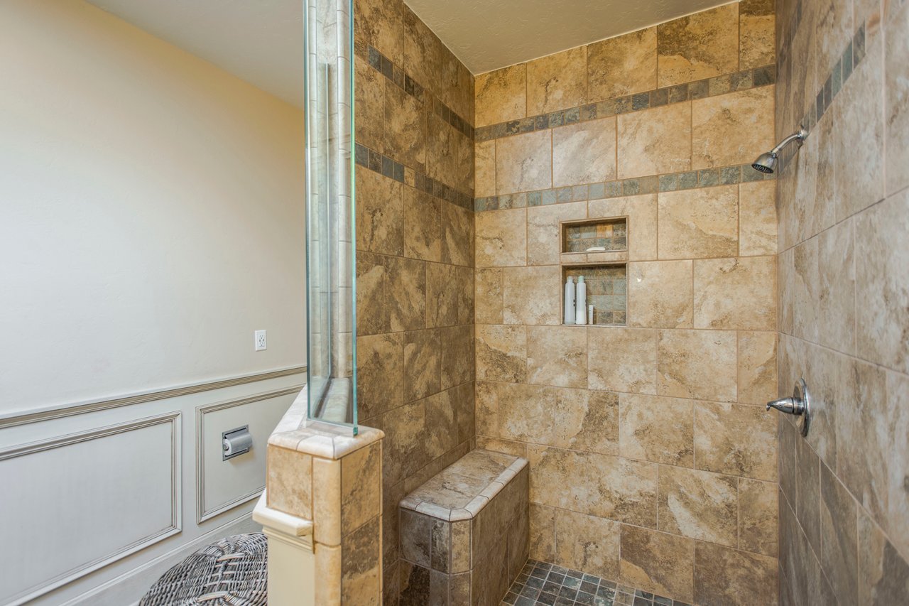 Walk-in shower with tan stone tile, a built-in bench, and glass partition.
