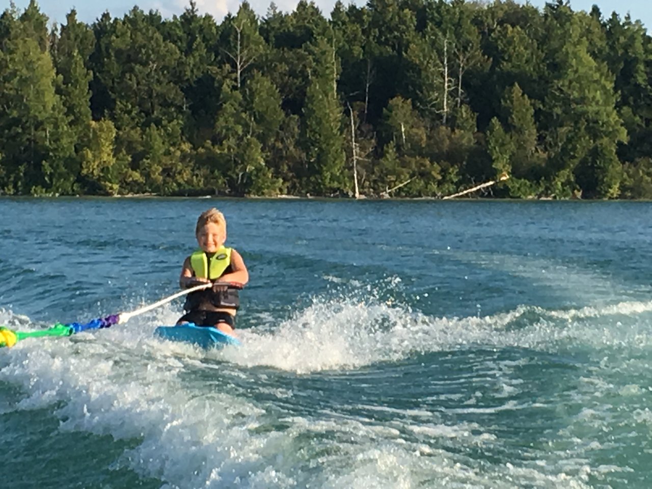 A young boy kneeboarding behind a boat rental in Benzie County