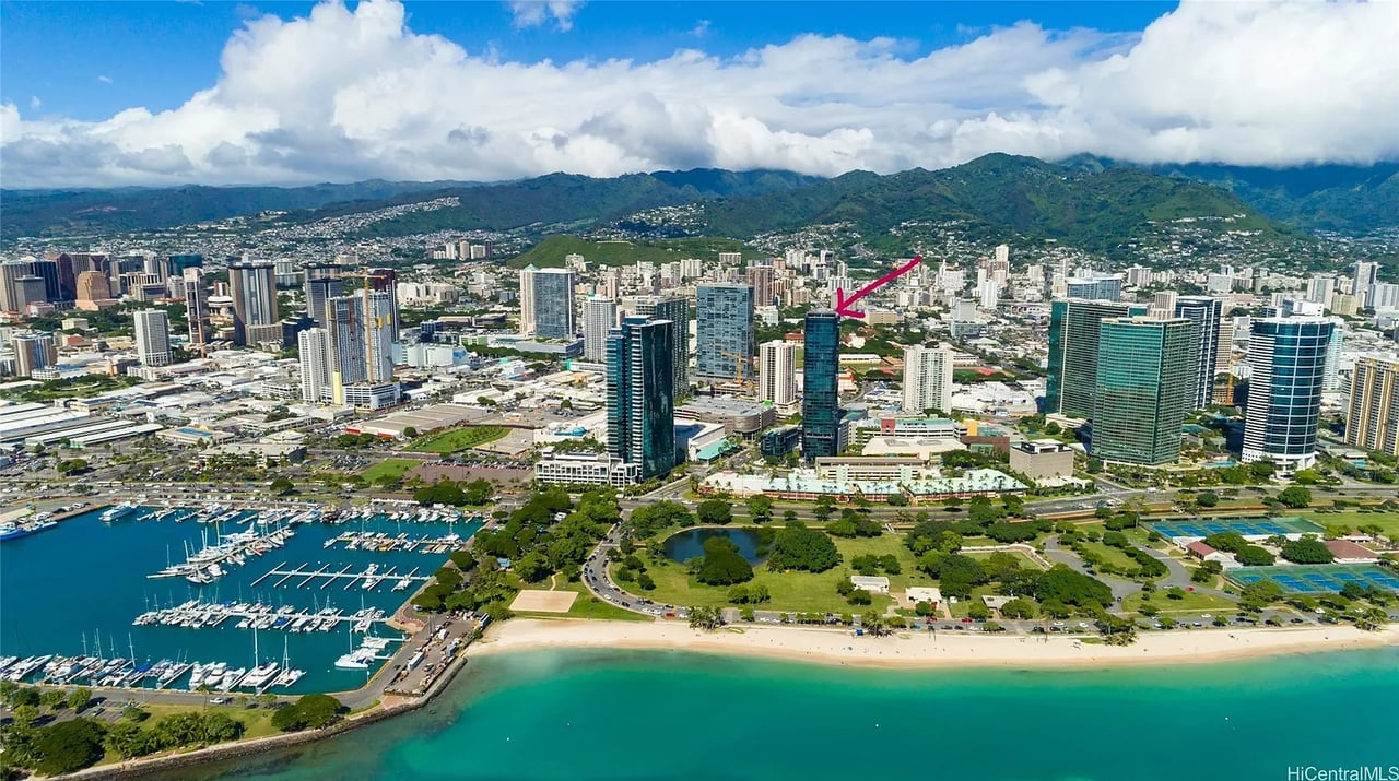Aerial view of Honolulu’s waterfront and skyline, with a magenta arrow marking a high-rise.