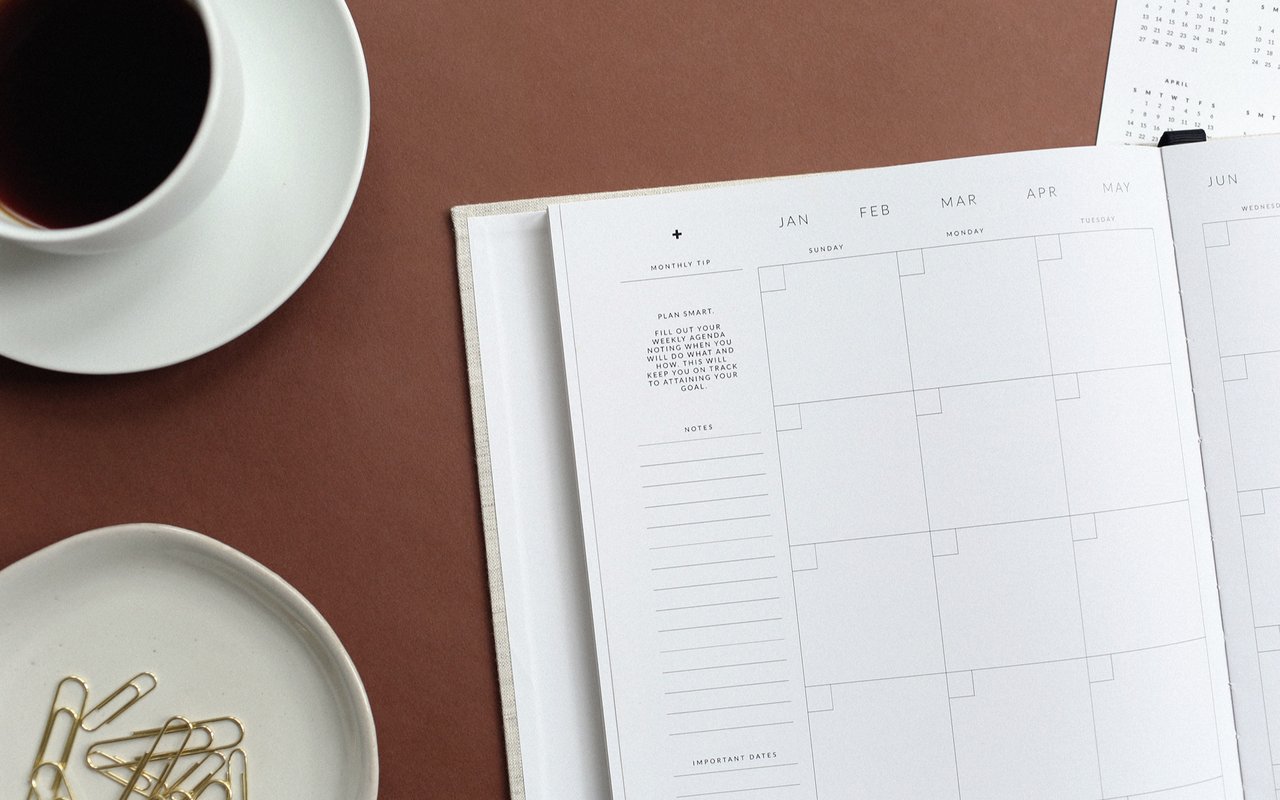 Monthly planner beside black coffee and gold paper clips on a dish.