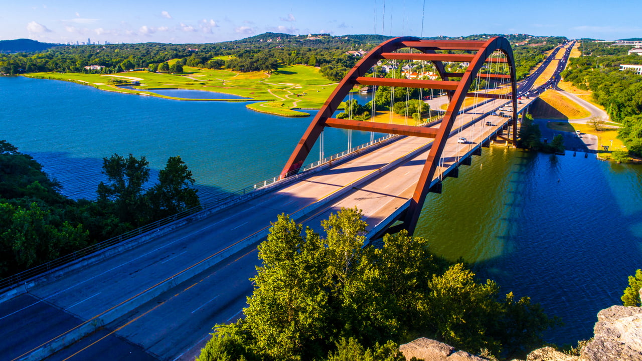 Pennybacker Bridge crosses Lake Austin, surrounded by green hills.