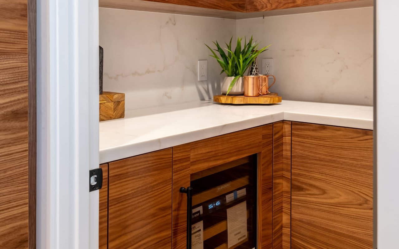 Built-in wine cooler beneath wood cabinetry, with a plant and copper mug on the counter.