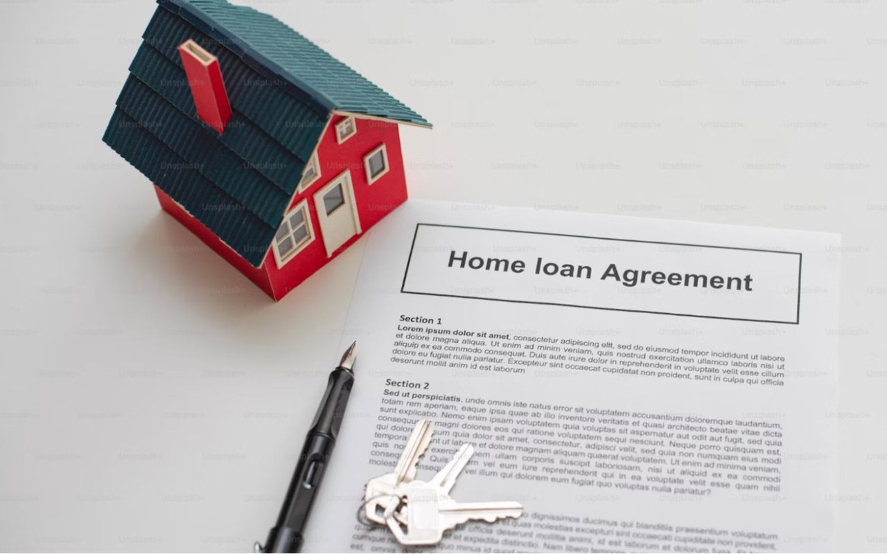 Home loan agreement with pen, keys, and model house on table.