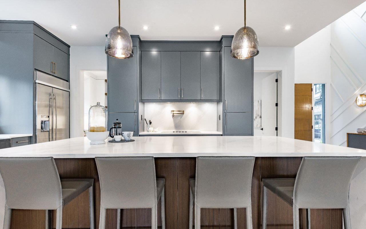 Modern kitchen with slate-blue cabinets, a large white island, and metallic pendant lights.