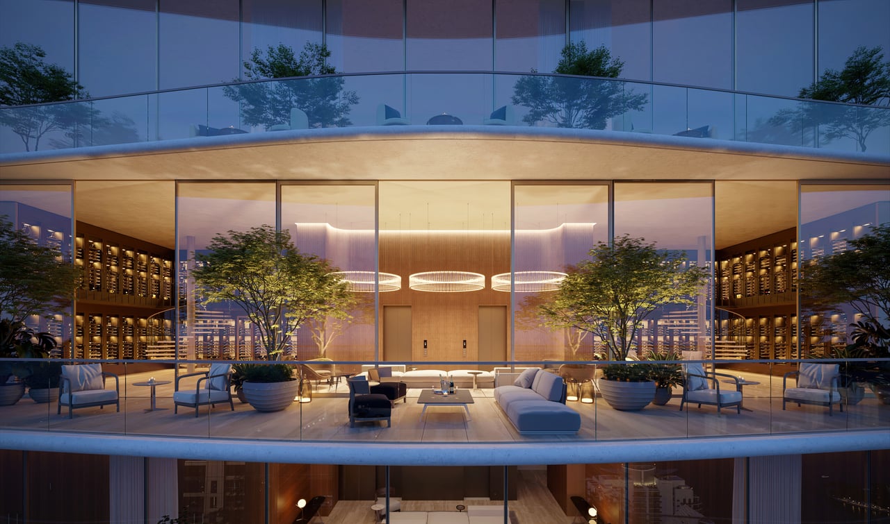 Curved glass tower facade with a furnished terrace, planters, and warmly lit interiors at dusk.