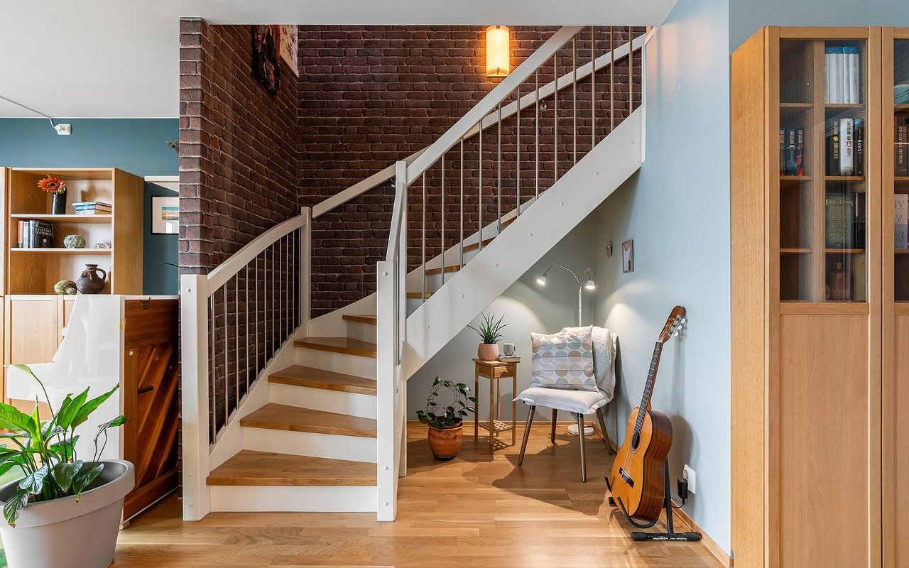 Furnished interior with a white wood-tread staircase, exposed brick wall, and small seating area.
