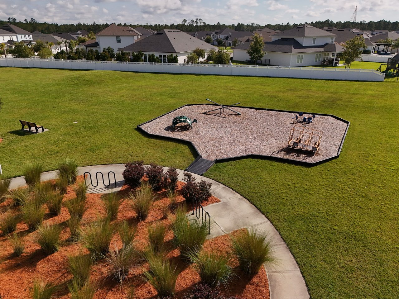 Neighborhood playground with a wood-chip play area, broad lawn, and homes in the background.