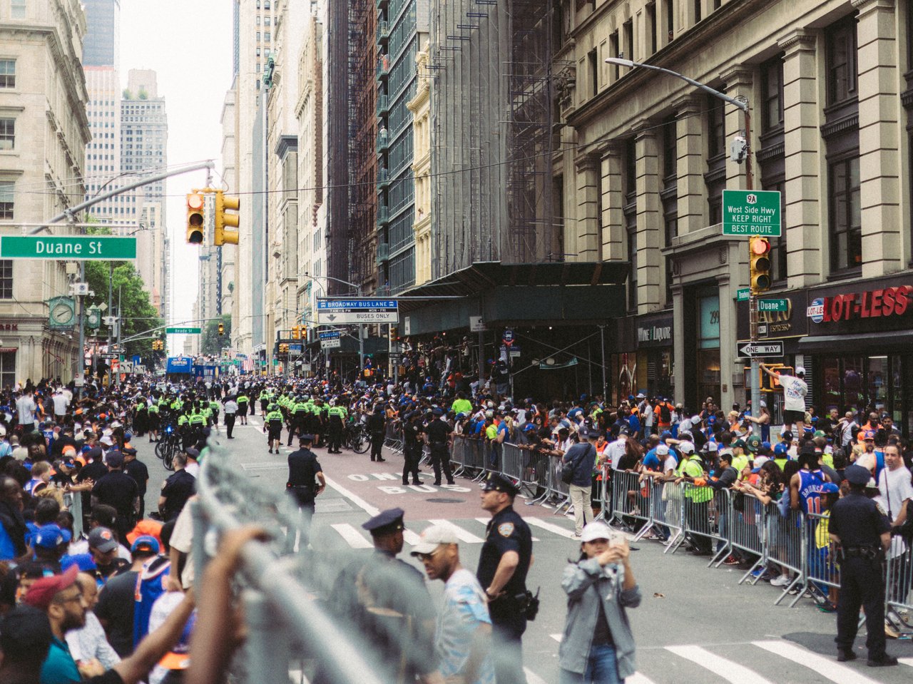 A panoramic aerial photograph of thousands of New York City Marathon runners crossing the Verrazzano-Narrows Bridge, with New York Harbor, the bridge's suspension towers, and the Brooklyn shoreline visible.