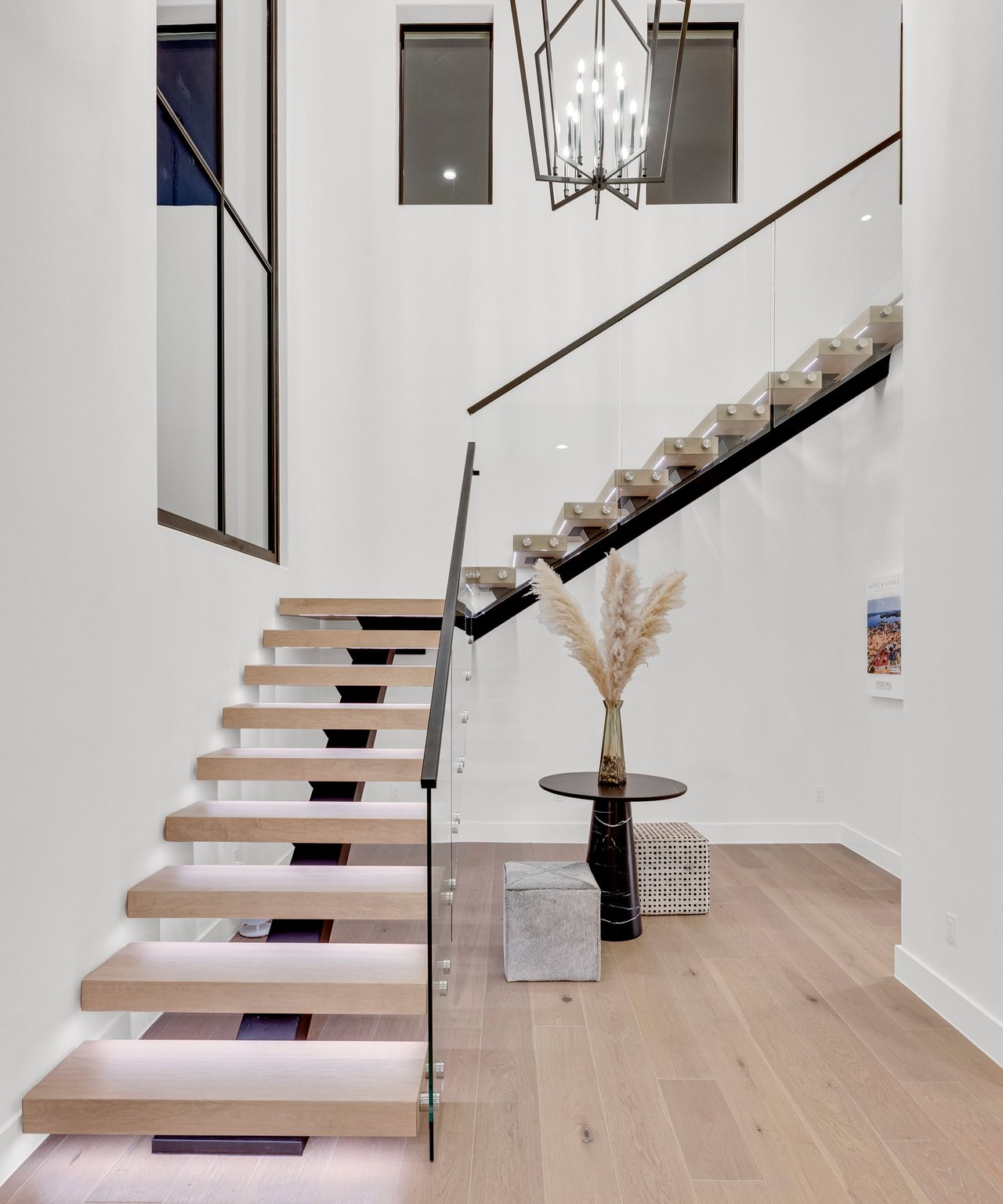 Modern entryway with a floating wood staircase, glass railing, and geometric chandelier.