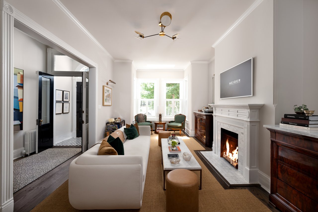 Living room with a white sofa, lit fireplace, and bright bay windows with shutters.