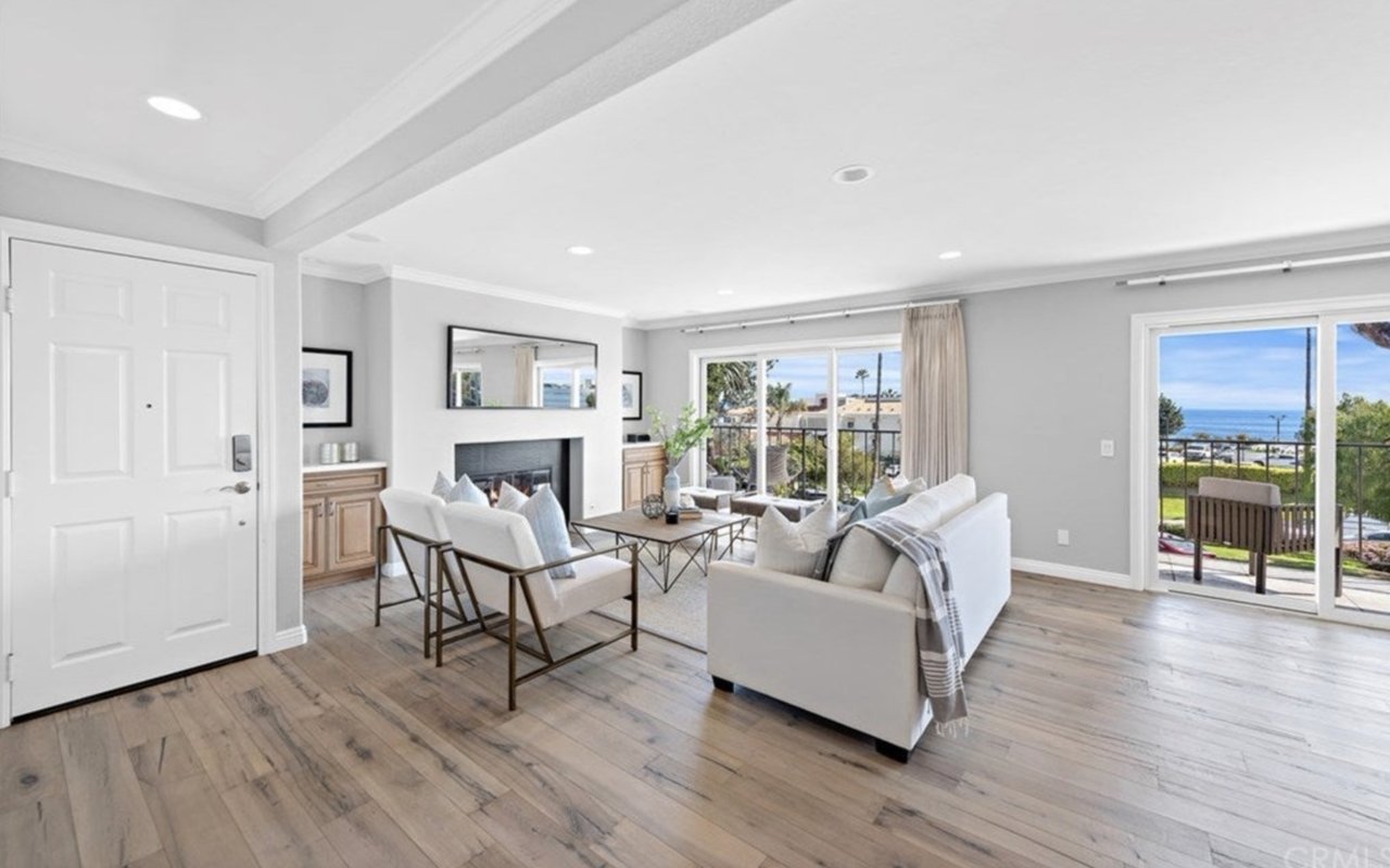 Furnished living room with a fireplace, white sofas, and sliding doors overlooking the ocean.
