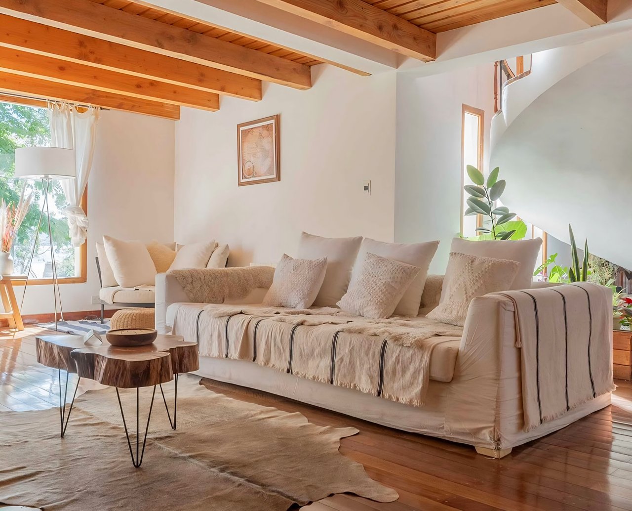 Living room with cream sofas, exposed wood ceiling beams, and sculptural wood coffee tables.