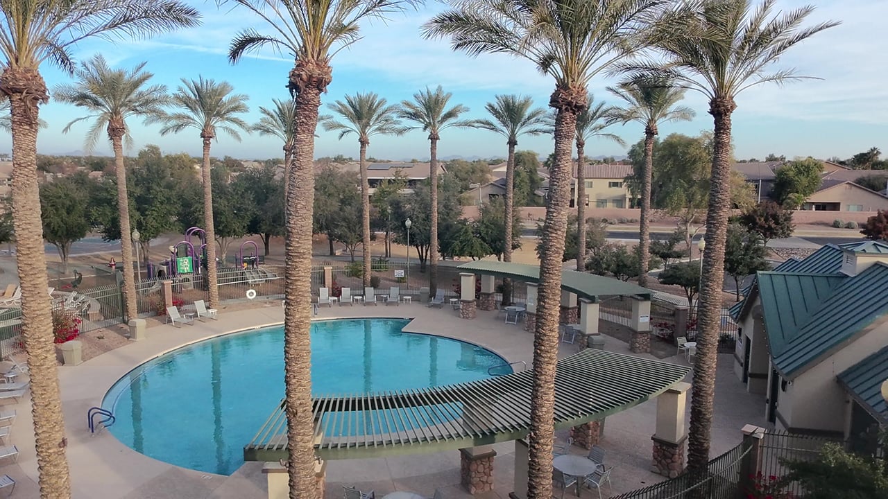 Community pool with palm trees, a fenced playground, and shaded pavilion.