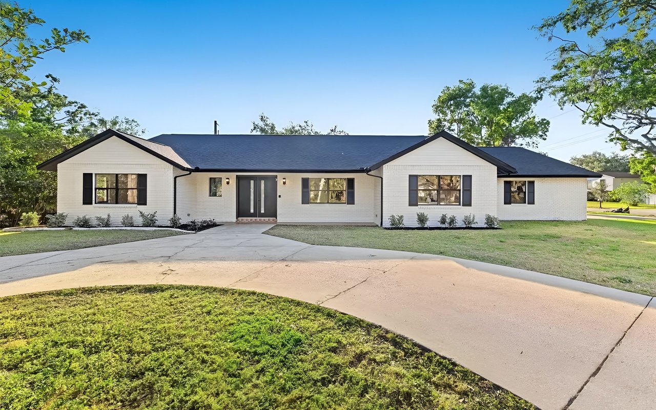 Single-story white house with a dark roof, black shutters, and a curved driveway.