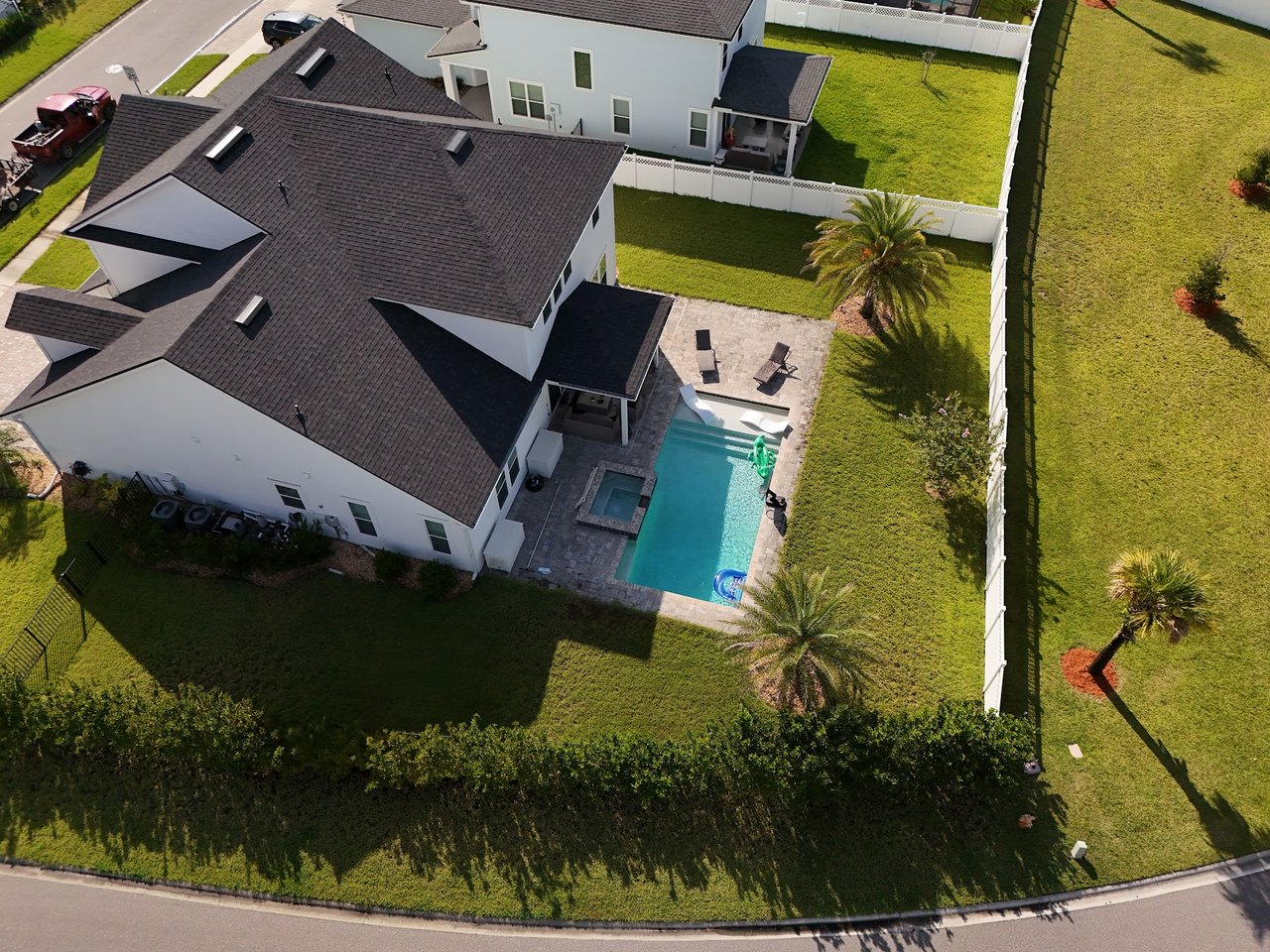 Aerial view of a white two-story home with a fenced backyard pool and paved patio.