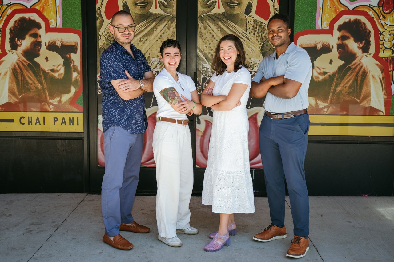 Four smiling team members pose outside a storefront covered in colorful illustrated murals.