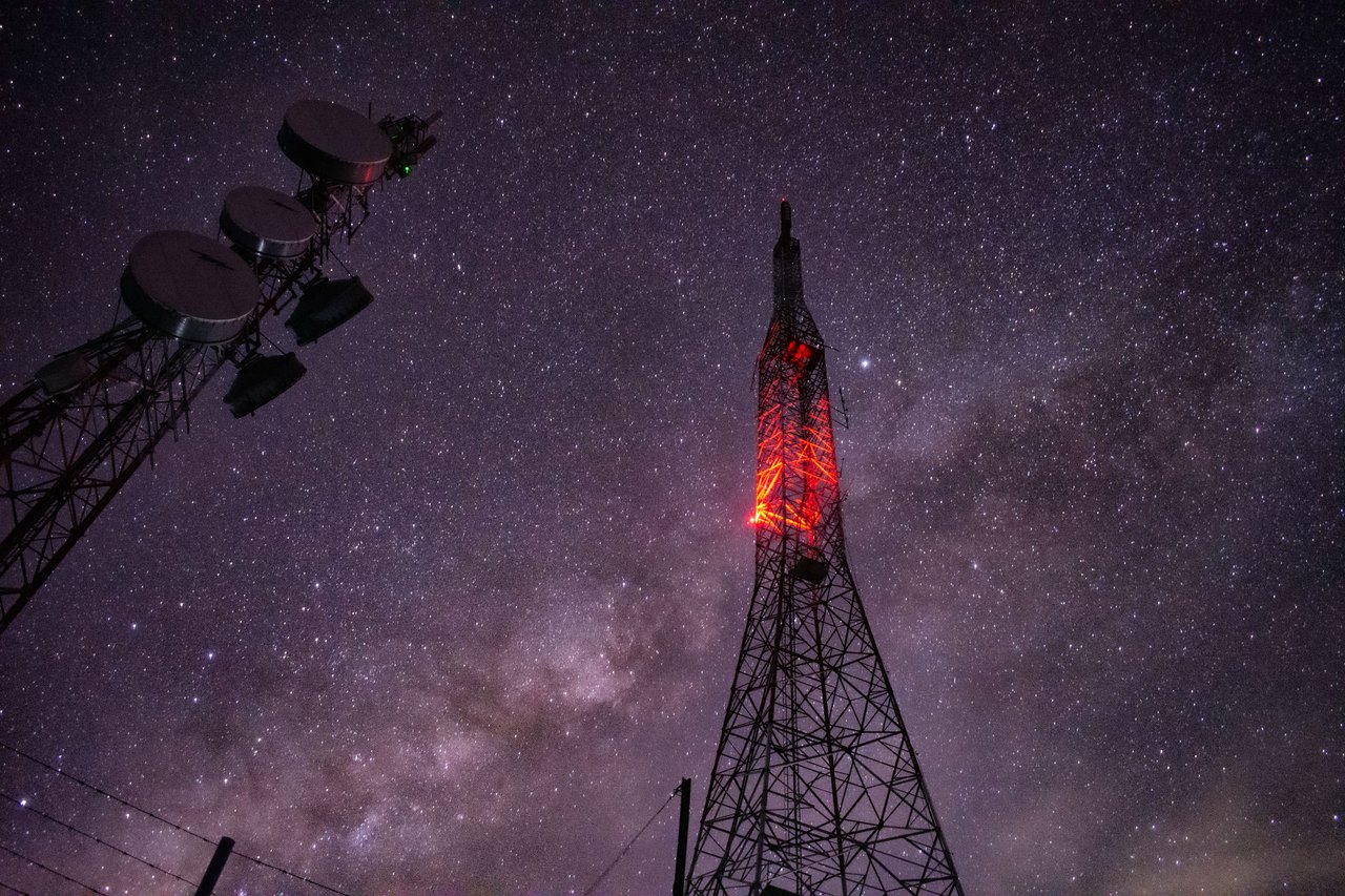 Radio towers silhouetted against the Milky Way, with one tower glowing red.