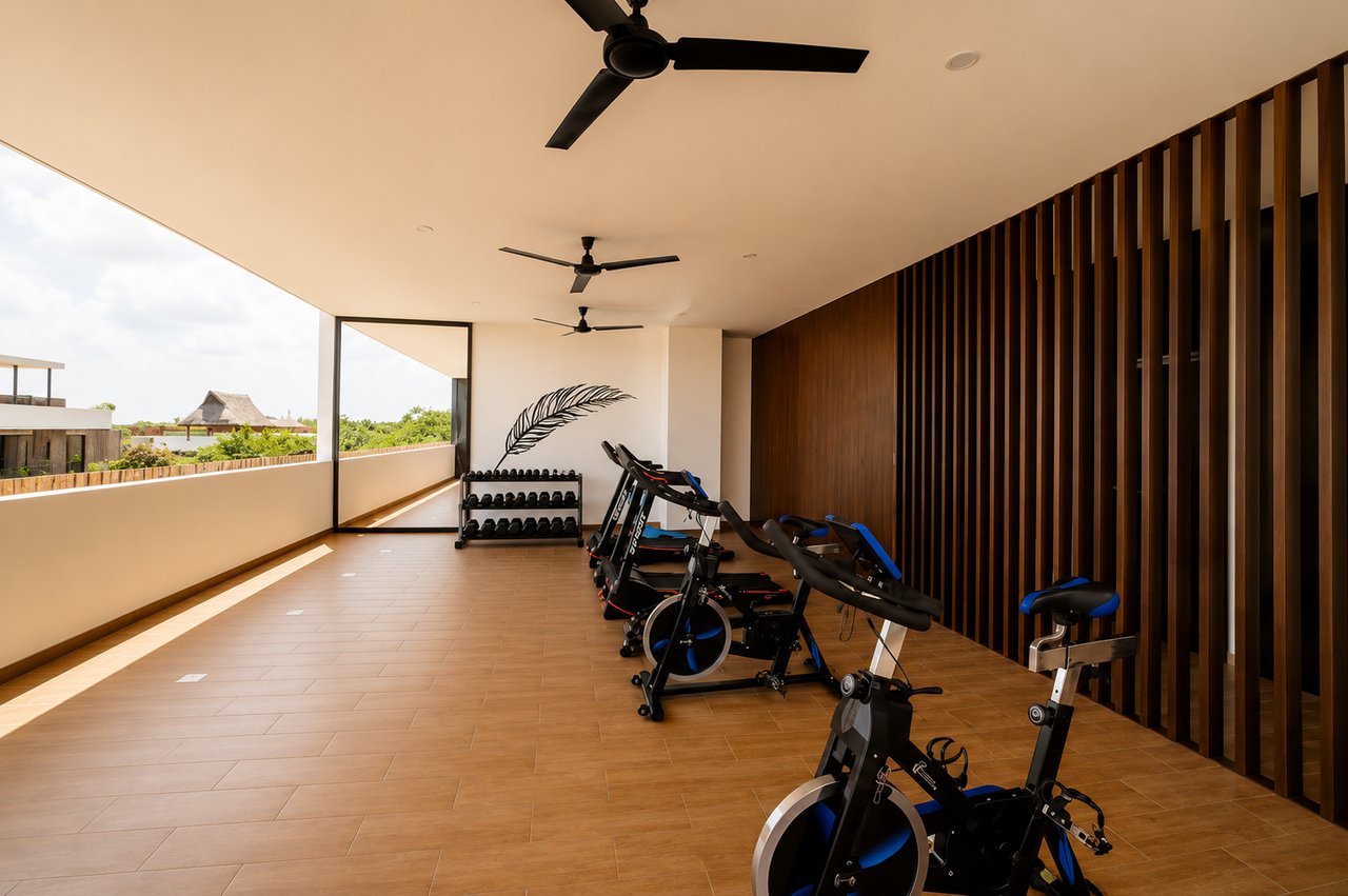 Fitness room with stationary bikes, treadmills, and weights beside an open balcony.