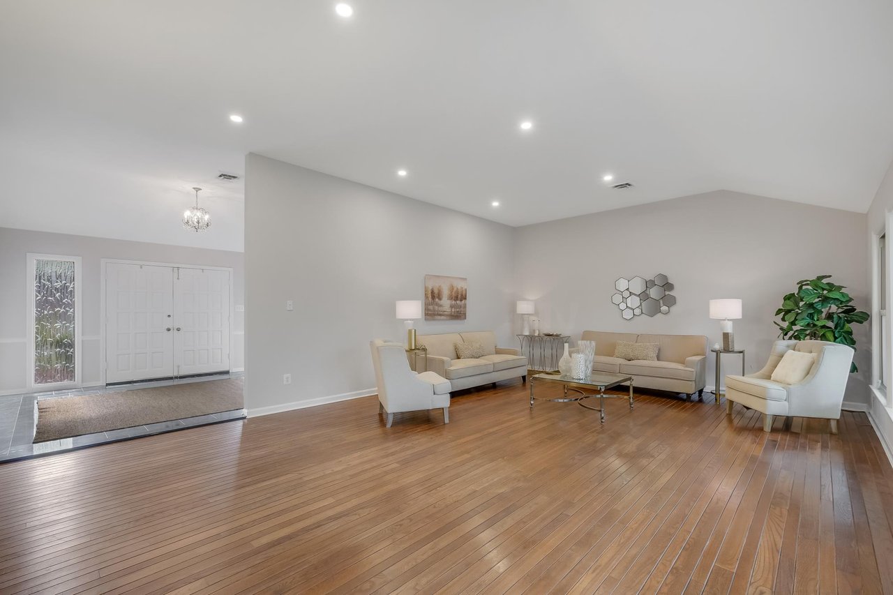 Staged living room with polished wood floors, beige sofas, and a glass coffee table.