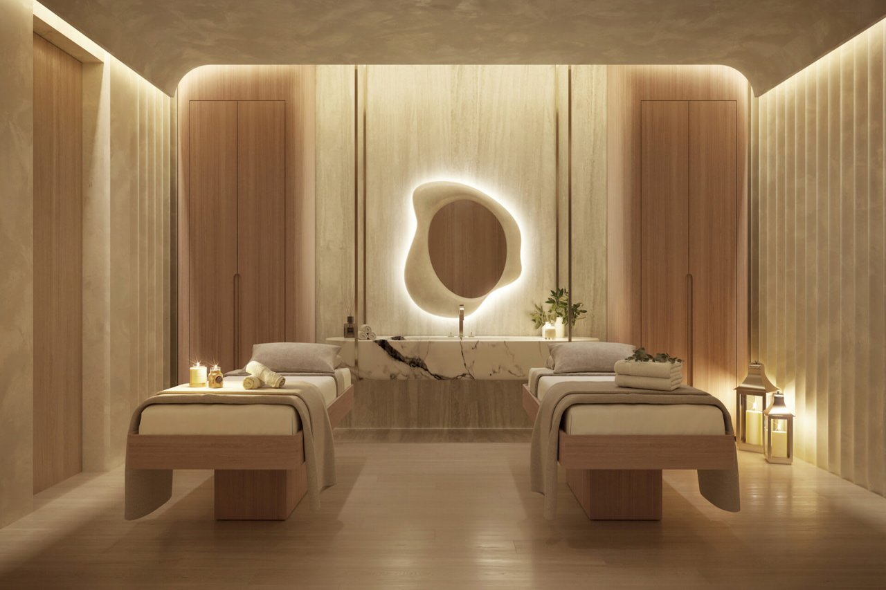 Spa treatment room with two massage tables and an illuminated sculptural mirror.