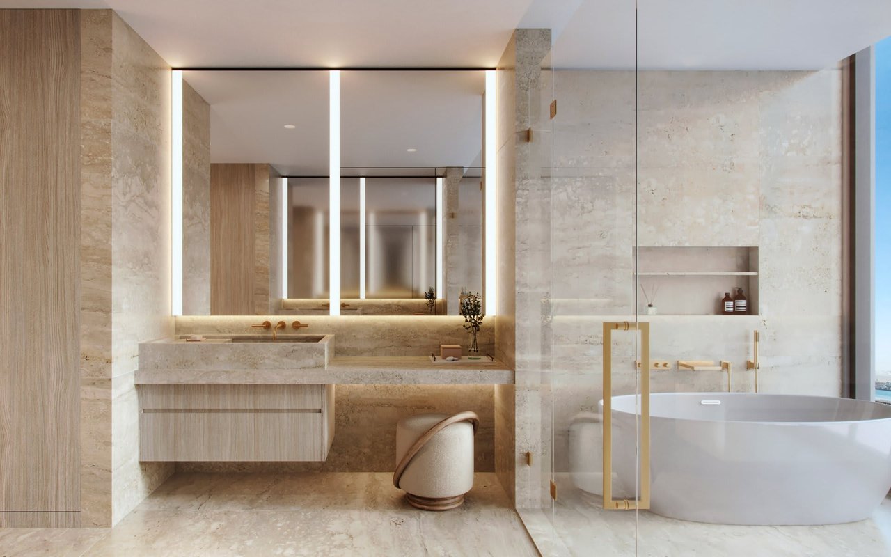Luxury stone bathroom with an illuminated vanity mirror, gold fixtures, and a freestanding bathtub.