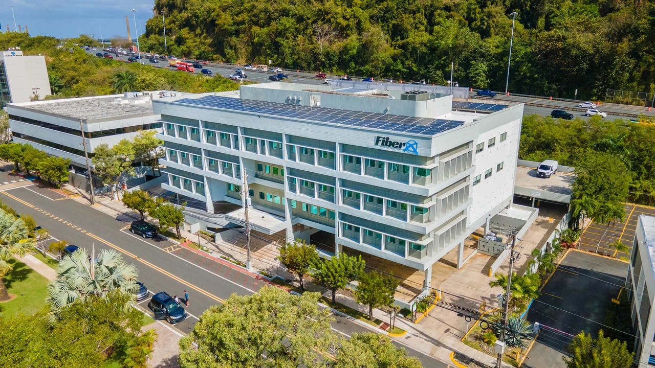 Aerial view of Lot 6 at Metro Office Park, showcasing a multi-story office building with solar panels on the roof, adjacent parking spaces, and a nearby highway.
