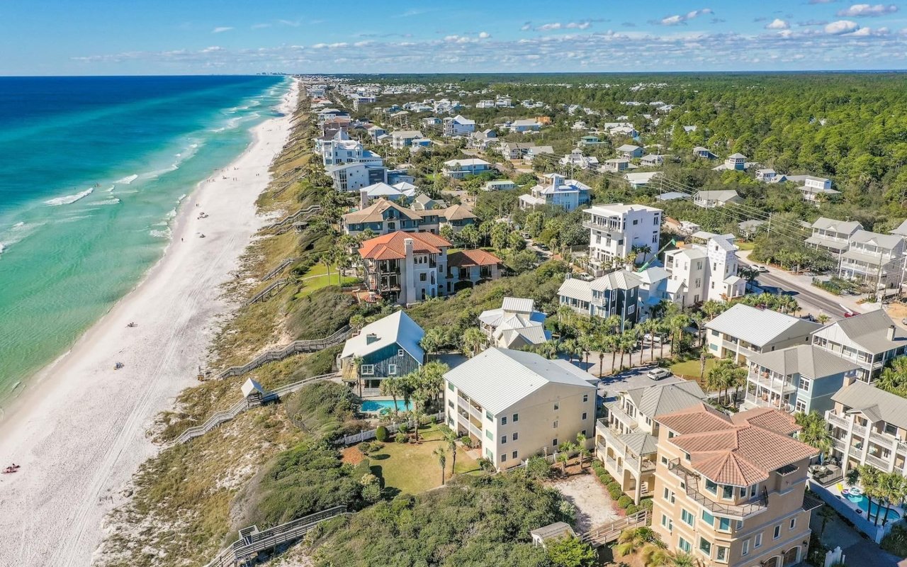 An aerial view of a coastal community with white sand beaches, turquoise water, and upscale homes.