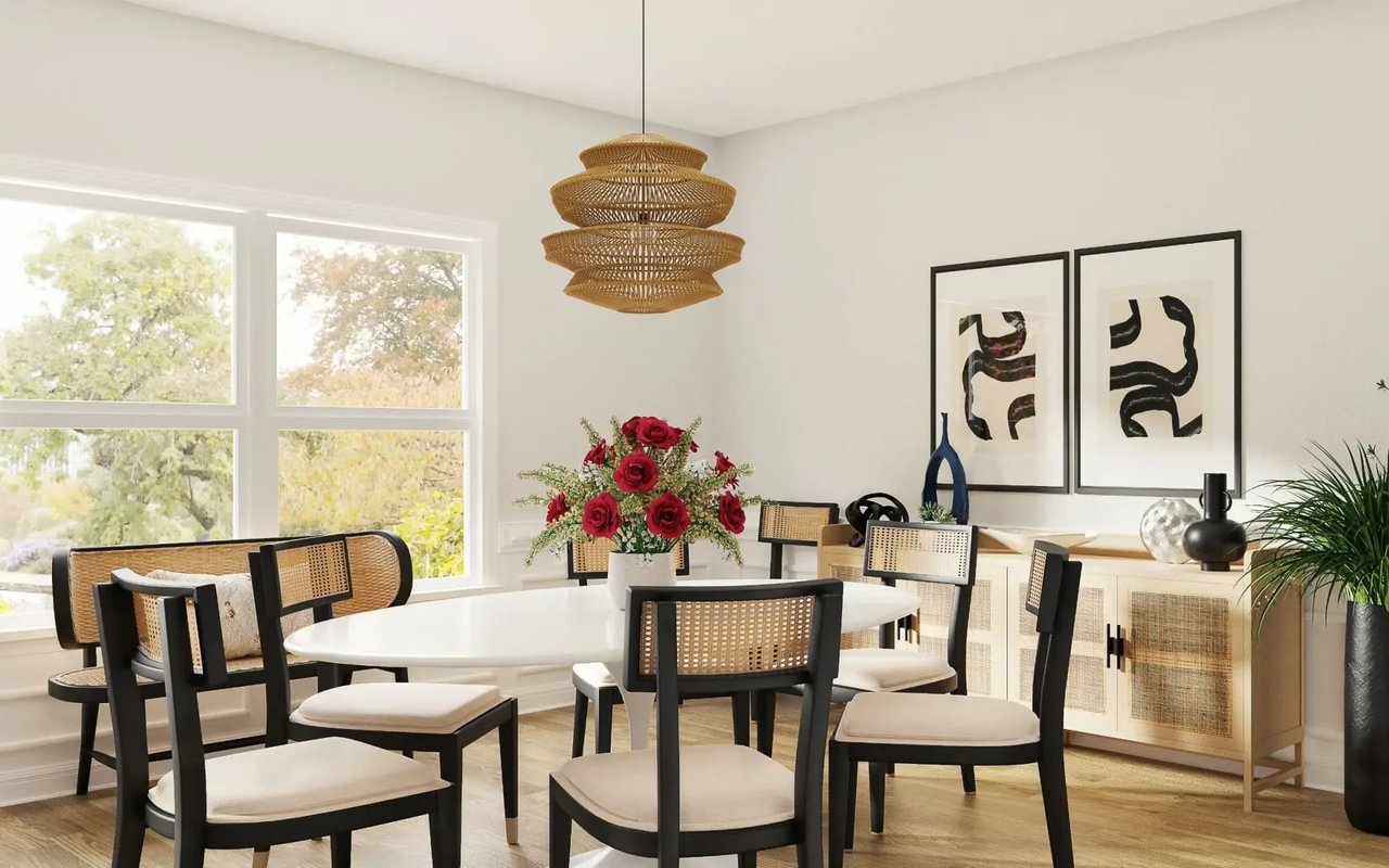 A dining room featuring a white oval table, rattan chairs, a woven pendant light, and abstract wall art.