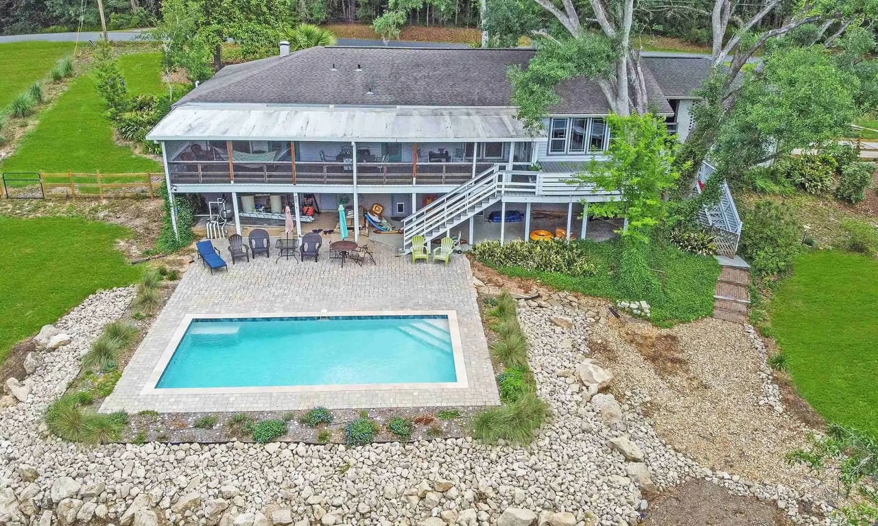  An aerial view of a property with a swimming pool in the backyard. The house has a large patio area, surrounded by greenery, suggesting a comfortable and luxurious living space.