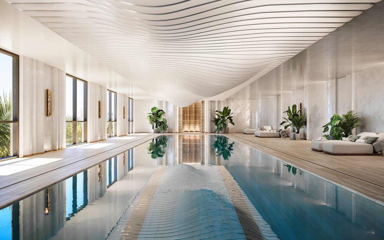 Indoor swimming pool beneath a sculptural white ceiling, with marble walls and loungers.