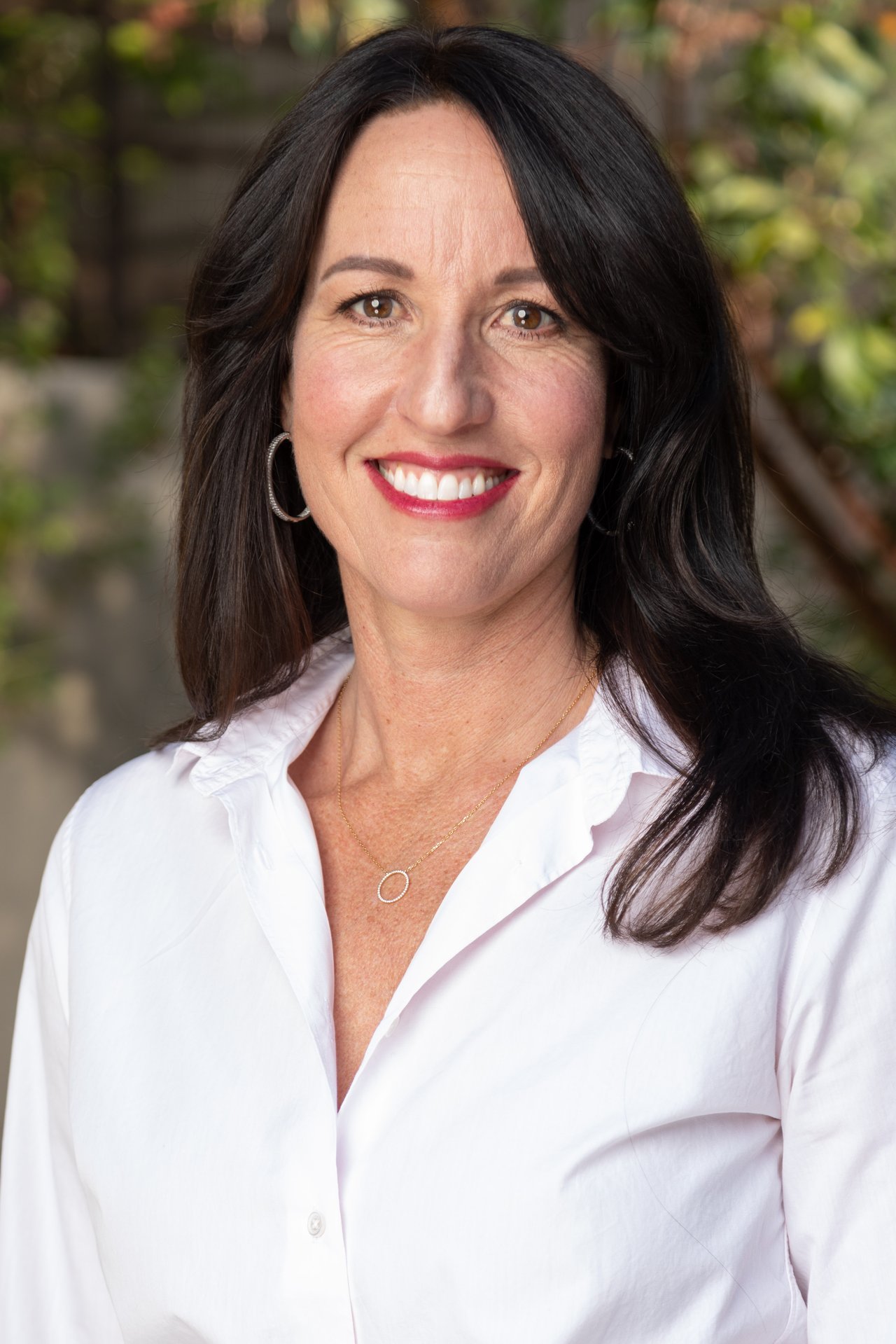 Michelle Ocheltree in a white blouse, smiling against a softly blurred green background.