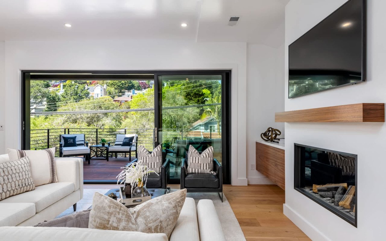 Living room with a linear fireplace and sliding doors opening to a deck with outdoor seating.