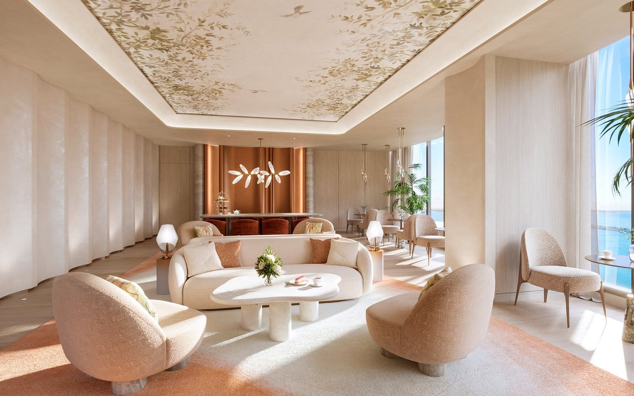 Luxury living room with cream seating, a floral ceiling, and water views through floor-to-ceiling windows.