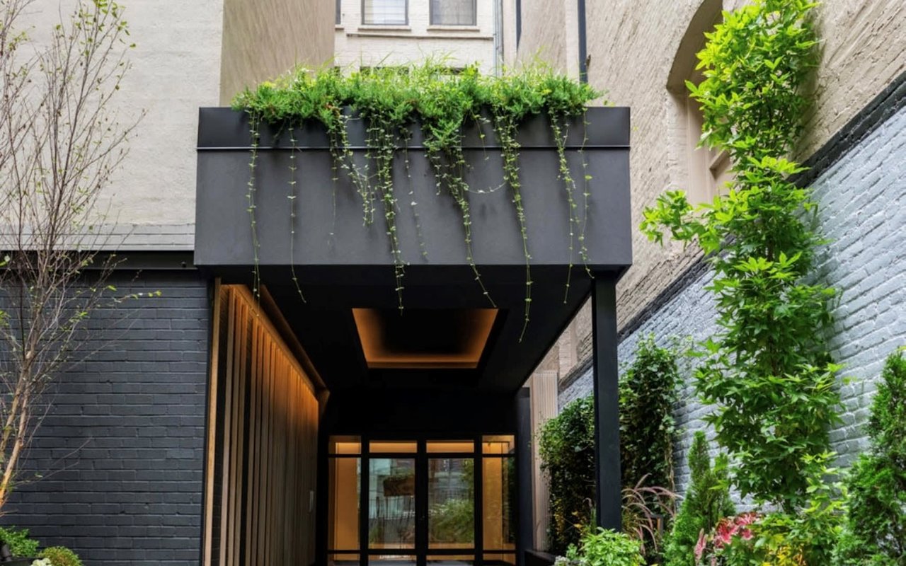 Building entrance beneath a planted black canopy, with brick walls and greenery.