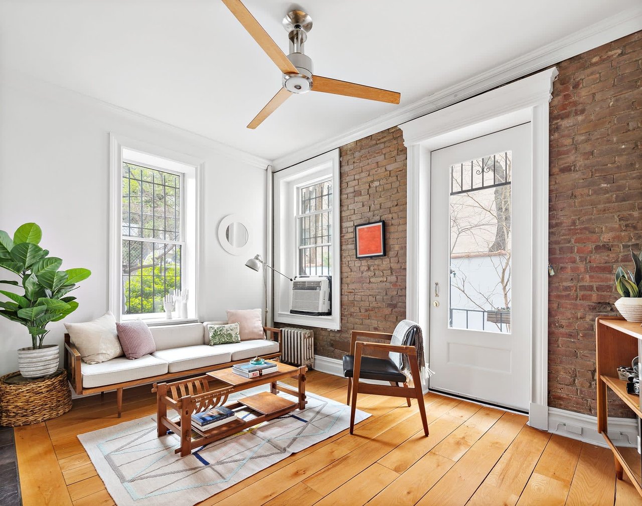 Furnished living room with exposed brick walls, tall windows, and honey-toned hardwood floors.