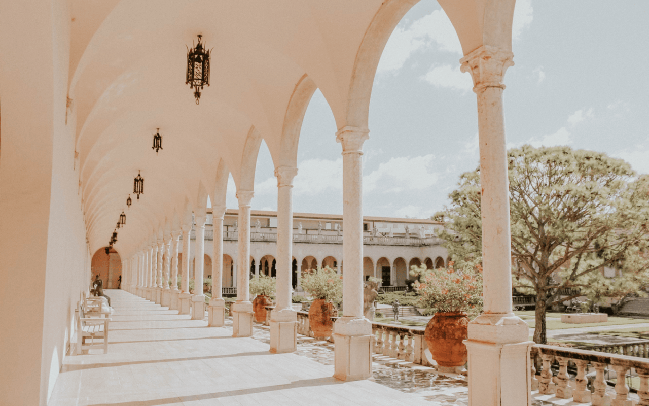  A long, elegant cloister with a series of light-colored arches and columns extends into the distance.