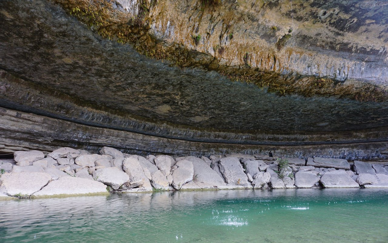 Turquoise water and pale boulders beneath a massive layered limestone overhang.