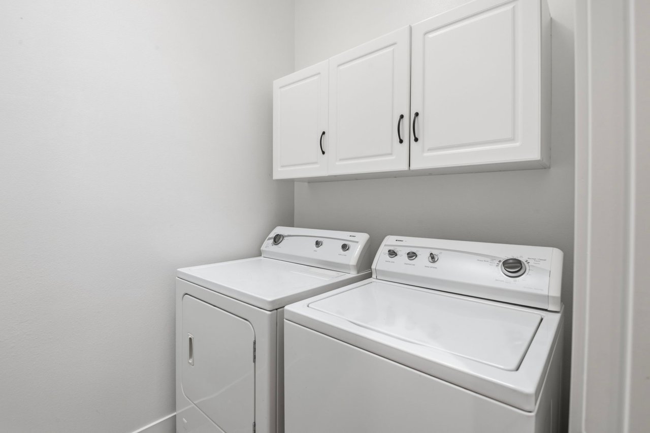 In-unit laundry area with full-size washer and dryer and upper storage cabinets