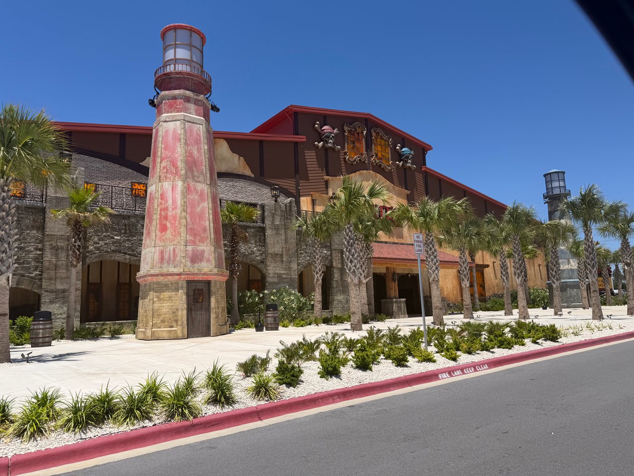 The pirate-themed exterior of the Pirates Voyage Dinner and Show building next to a tall, weathered brick lighthouse.