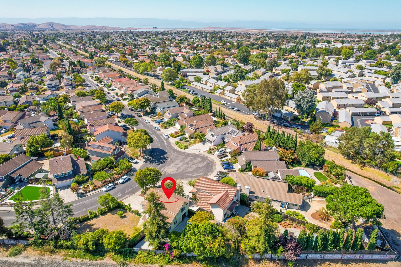 Aerial neighborhood view with a red marker over a house near a cul-de-sac and bay in the distance.
