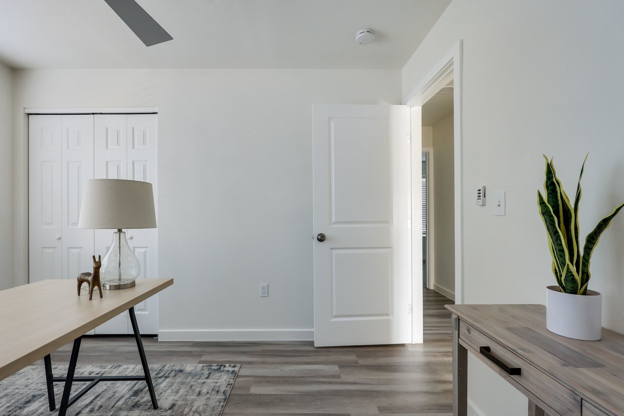 Furnished room with a desk, double closet doors, and an open doorway to the hall.