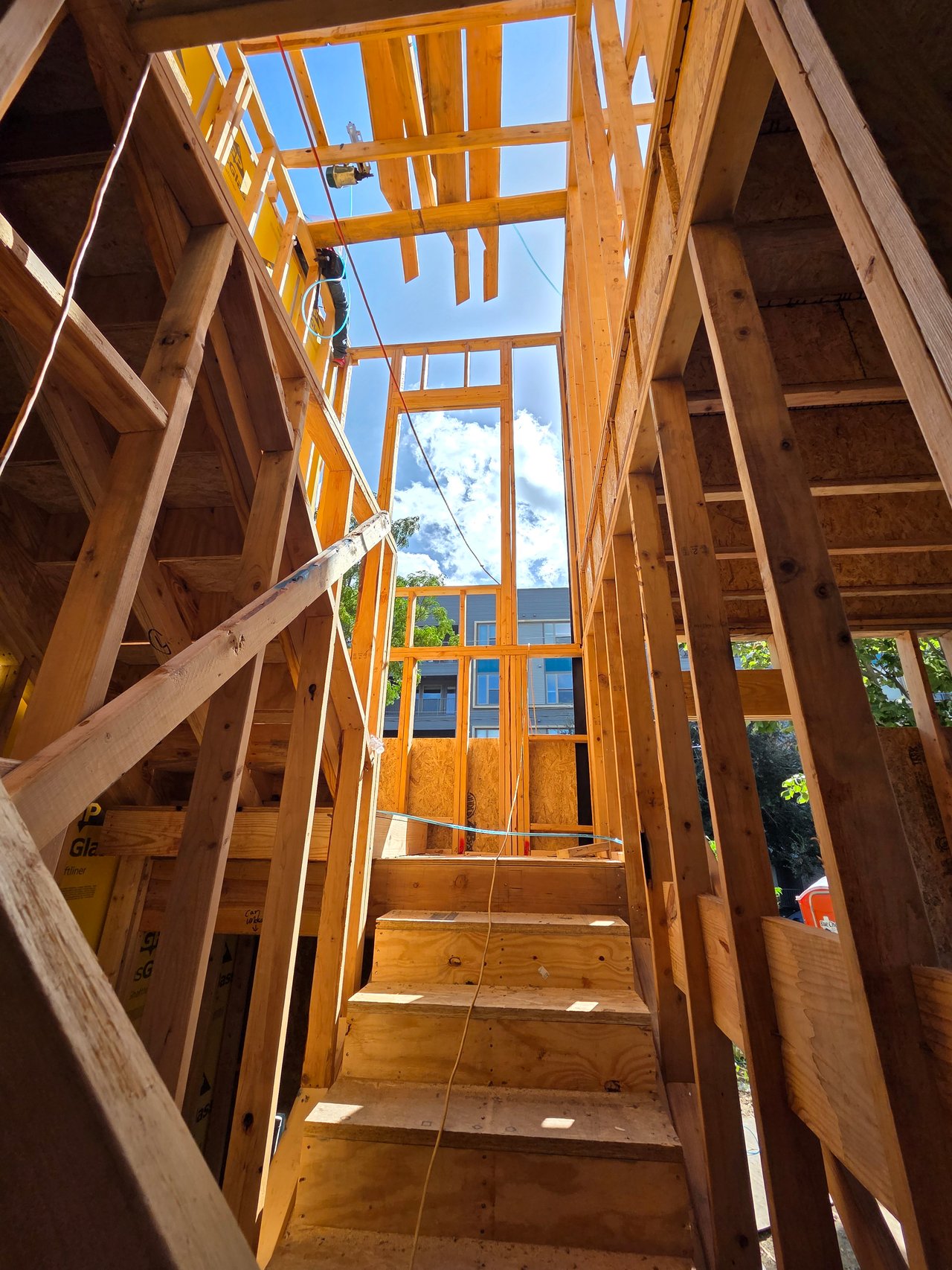 Unfinished wooden staircase surrounded by exposed framing, with blue sky visible through the open structure.