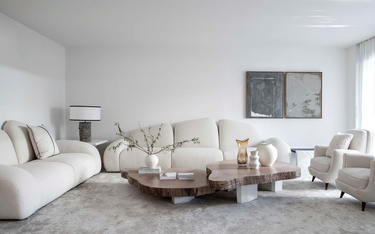 Modern living room with white seating, sculptural wood coffee tables, and abstract wall art.