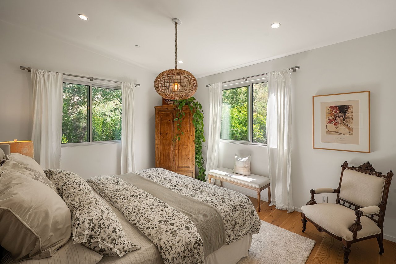 Bedroom with floral bedding, a wooden armoire, and windows overlooking greenery.