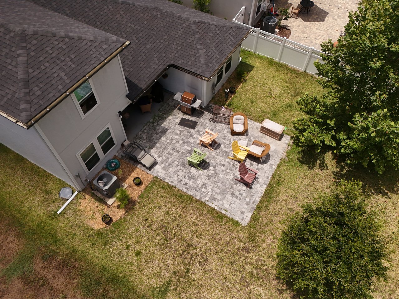 Aerial view of a backyard patio with colorful seating, a grill, and a fenced lawn.