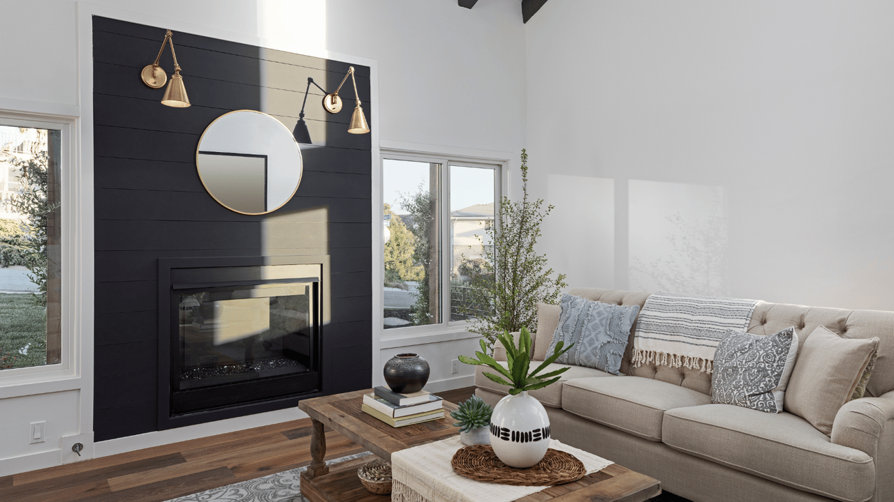 Living room with a black-paneled fireplace, round mirror, beige sofa, and wood coffee table.