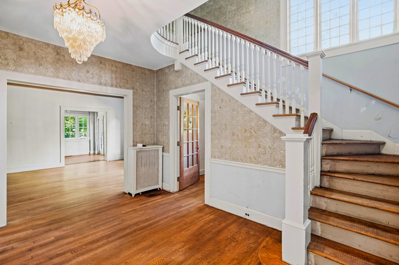 Foyer with a sweeping staircase, tall windows, polished hardwood floors, and a chandelier.