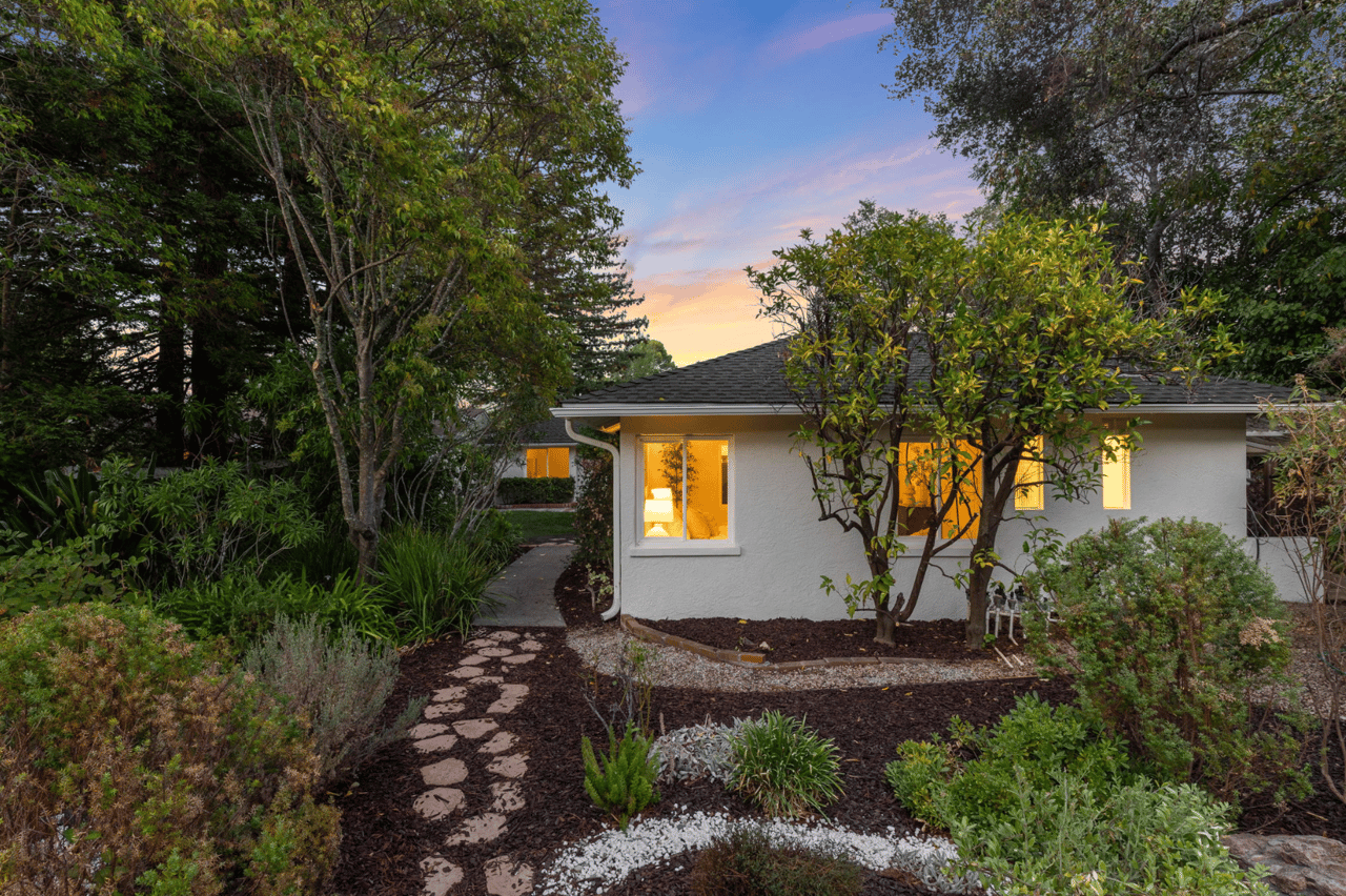 Single-story stucco home framed by mature landscaping and a stepping-stone path at dusk.