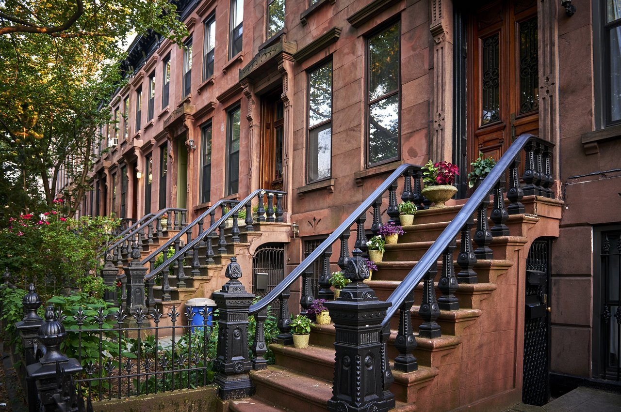 Brownstone townhouse row with ornate stoops, black iron railings, and flower pots.
