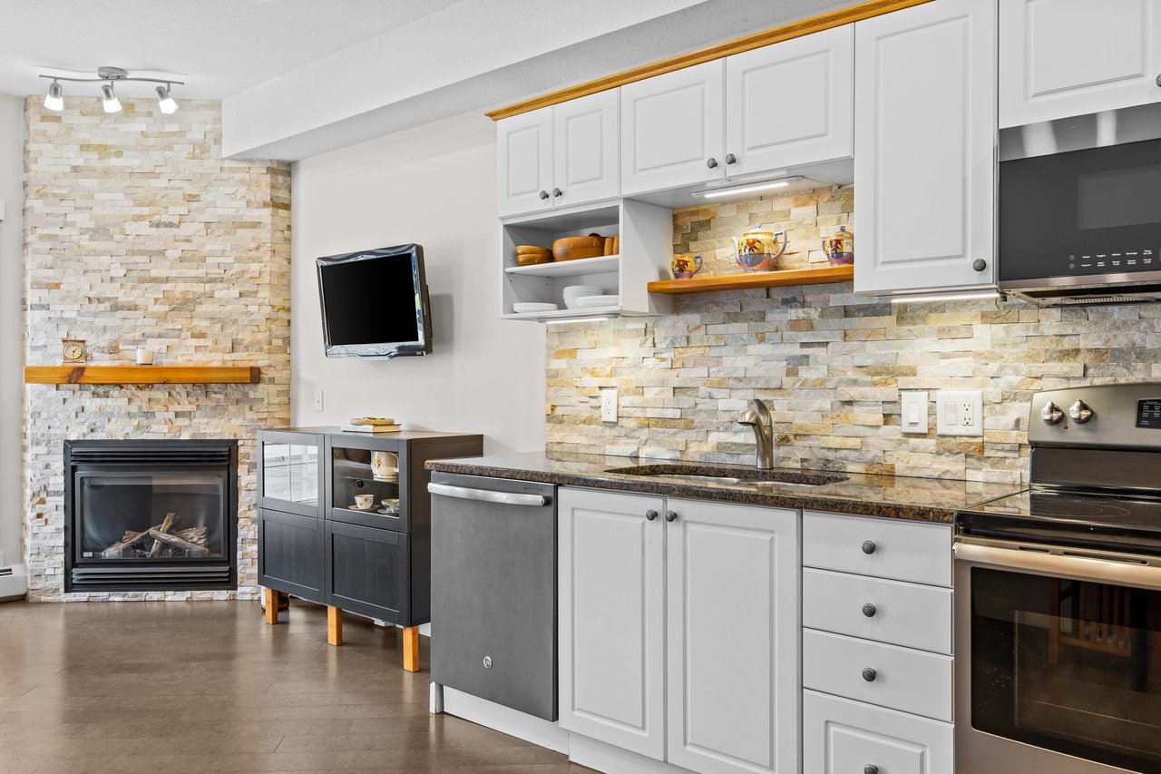 Kitchen with white cabinets, stone backsplash, and a fireplace with a wood mantel.